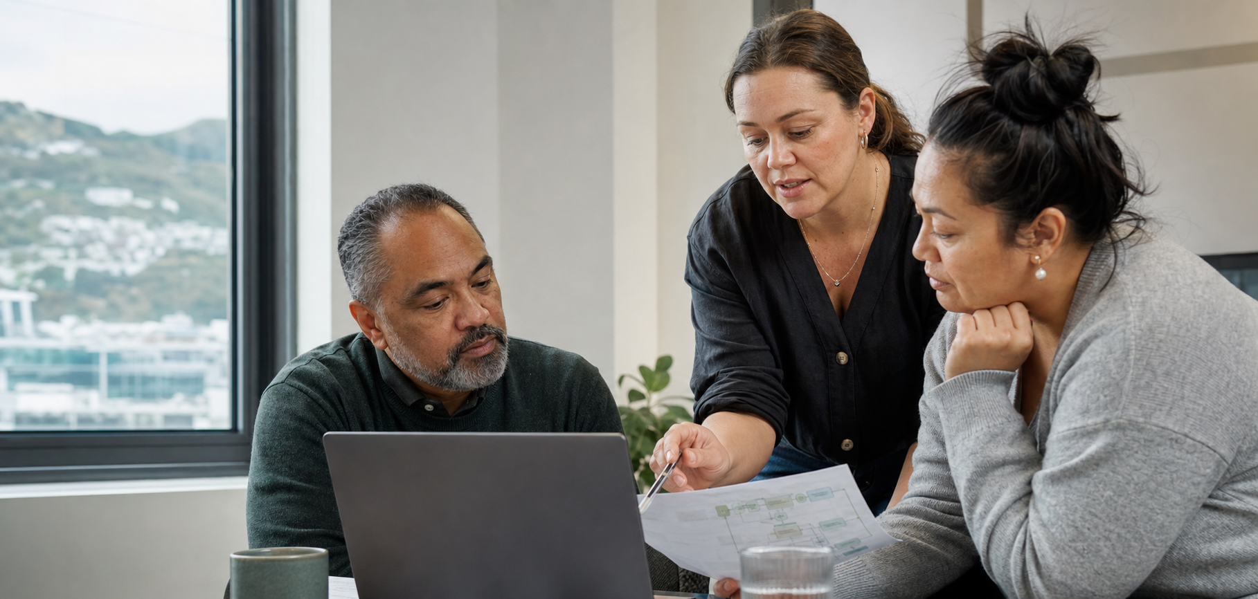 Three colleagues working together around a laptop and printed plans